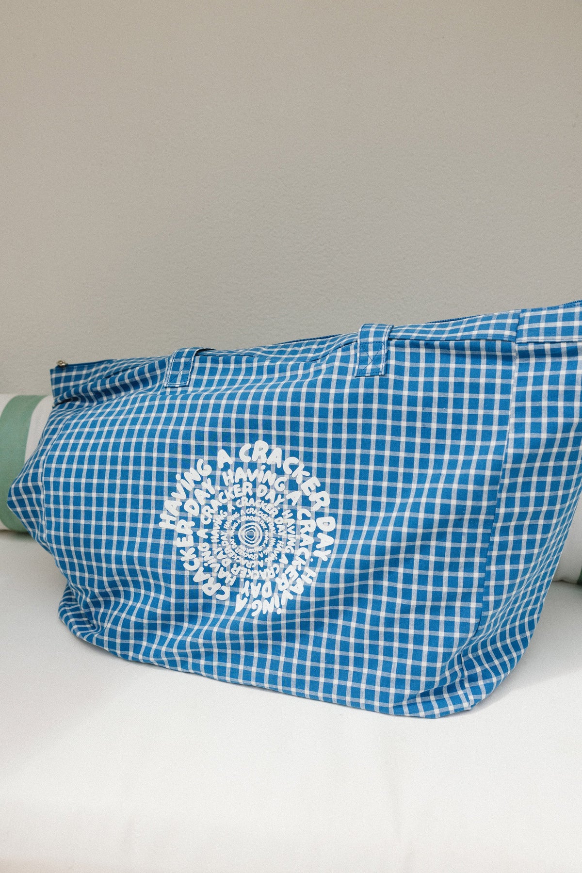 Blue checkered bag with a white having a cracker day design on a light gray background