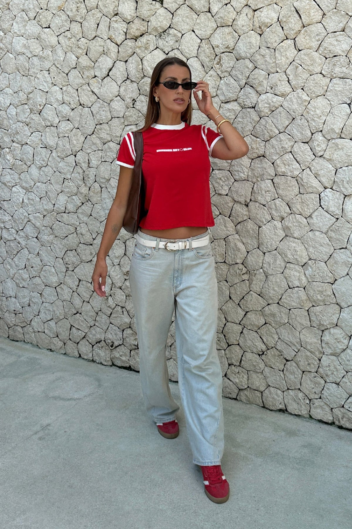 woman wearing a red racer baby tee by cracker day club with jeans walking down the street