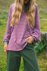 A woman wearing a pink and red striped long-sleeve top with dark green pants, standing outdoors in a grassy field.