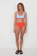 Woman wearing a light blue bikini bralette top and red high-waisted bottoms on a white background
