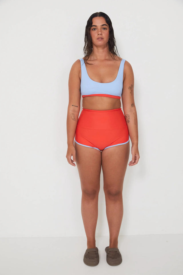 Woman wearing a light blue sports and swim bra and red swim shorts on a white background
