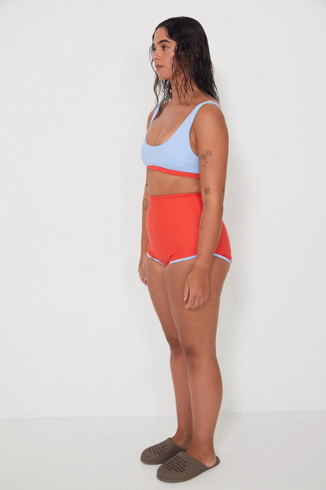 Woman wearing a light blue sports and swim bra and red swim shorts on a white background
