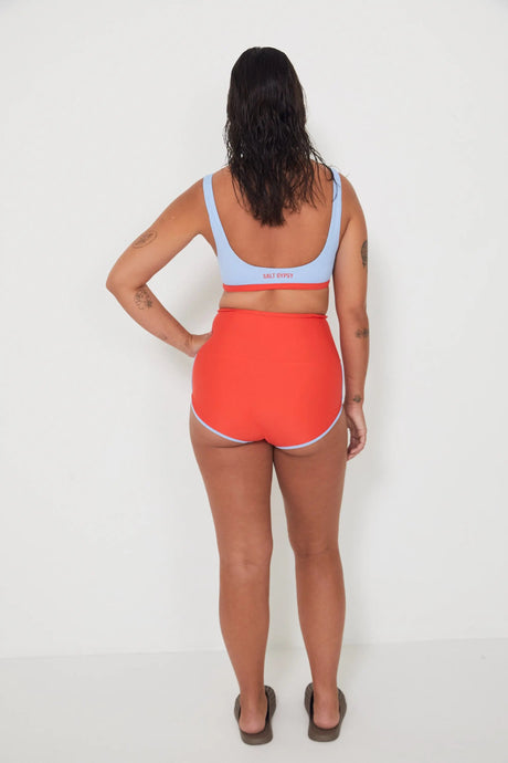 Person wearing a light blue sports and swim bralette and bright red swim shorts on a white background