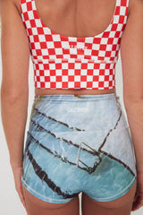 Person wearing a red and white checkered punchy surf crop top and blue shorts with graphic design.