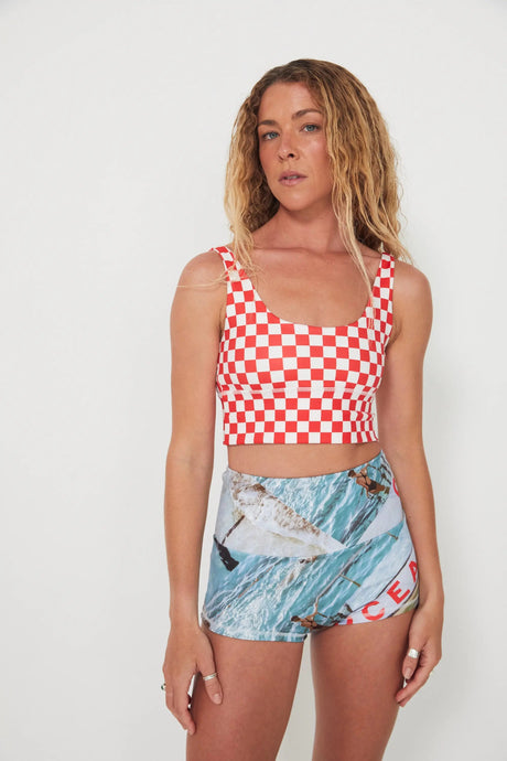 Woman wearing a red and white checkered punchy surf top and patterned ocean photographed shorts on a white background