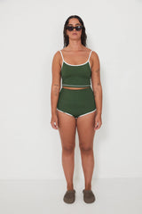 Woman wearing a green tankini surf top and betty bottoms 2.0 swimsuit with white trim against a white background