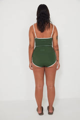 Woman wearing a green tankini surf top and betty bottoms 2.0 swimsuit with white trim against a white background