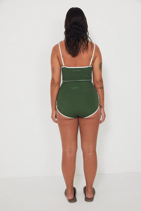 Woman wearing a green tankini surf top and betty bottoms 2.0 swimsuit with white trim against a white background