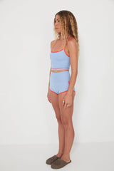 Woman wearing a light blue tankini surf top and betty bottoms 2.0 with red accents against a white background