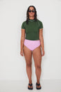 Woman wearing a green olive low rider rashguard and pink drifter swim bottoms with white trim on a plain background