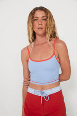 Woman wearing a light blue tankini surf top bra and red boarshorts on a white background