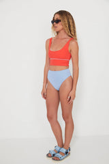 Woman wearing a red punchy bikini top and light blue high-waisted reversible drifter bottoms on a white background