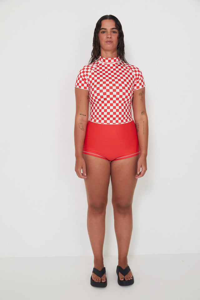 Person wearing a red and white checkered low rider rashugard top and red original betty bottoms shorts on a white background