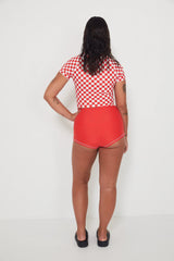 Person wearing a red and white checkered low rider rashguard and matching red original betty bottom shorts on a white background