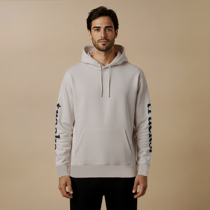 Man wearing a light gray hoodie with black text on sleeves against a beige background