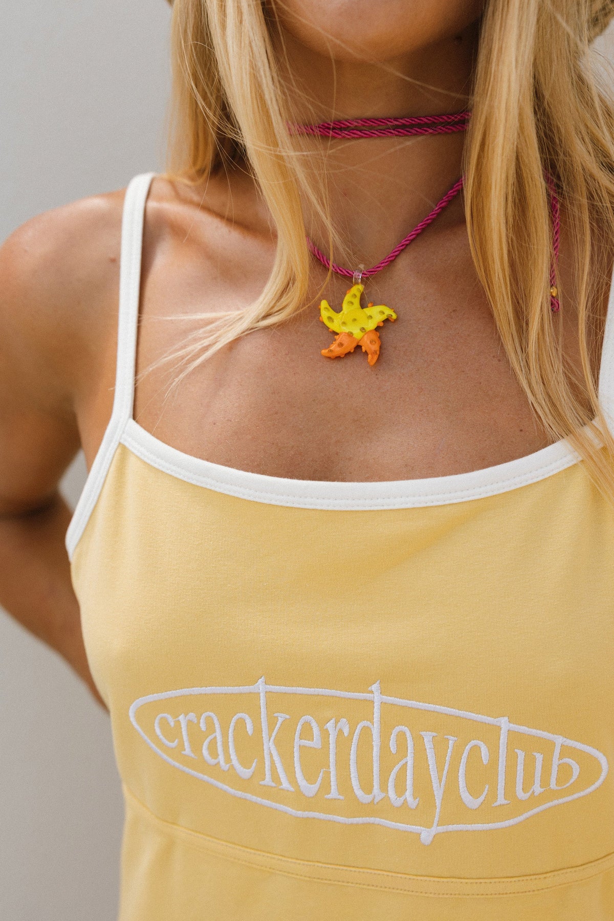 Woman wearing a yellow tank top with 'cracker day club' logo and a colorful necklace.