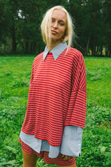 A woman standing outdoors in a grassy park wearing a red and white striped oversized tunic top with light blue and white striped collars and cuffs, paired with matching striped shorts.