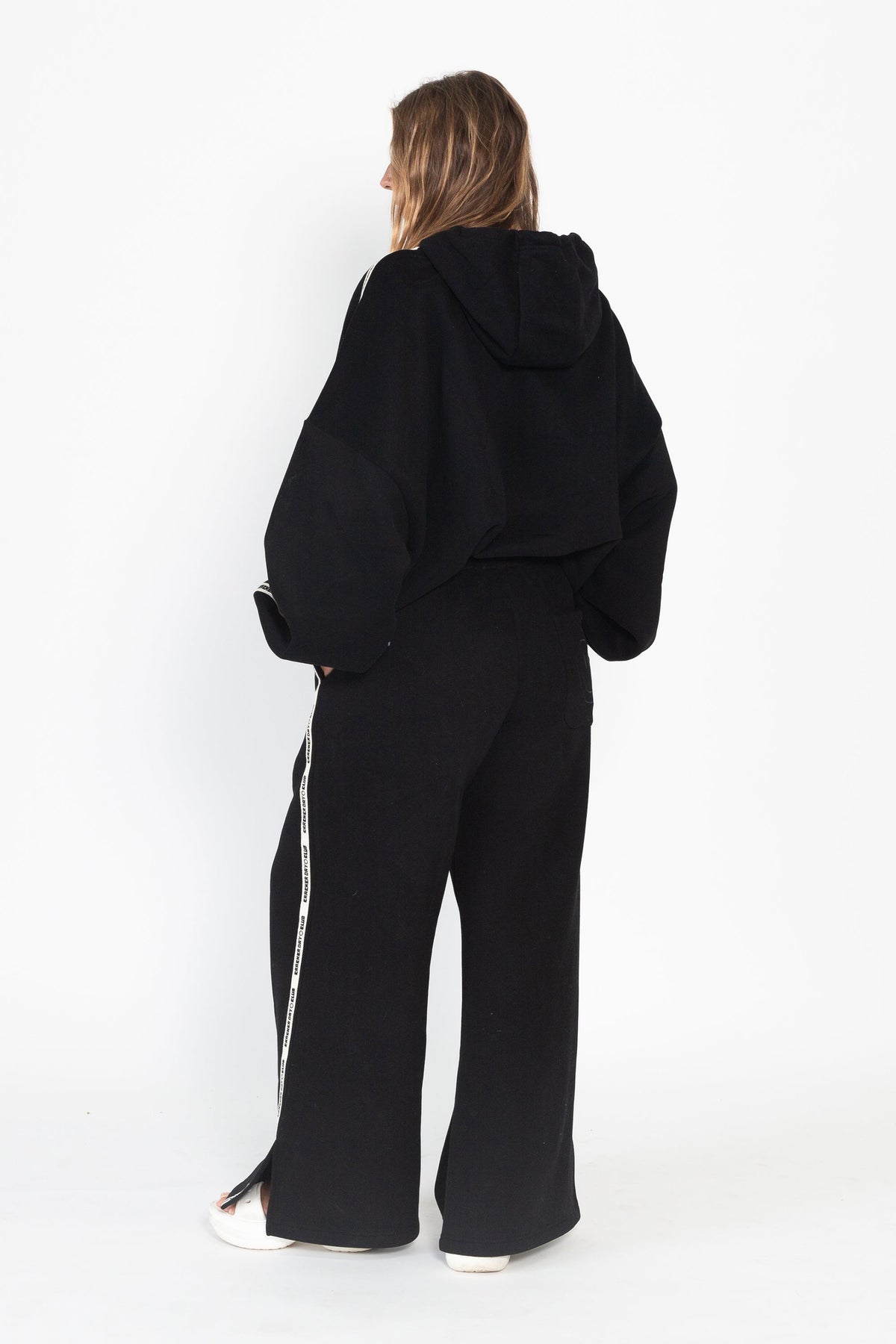 Person wearing a black hoodie and black pants on a white background