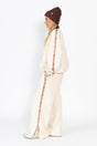 Person wearing a cream outfit with brown accents on a white background