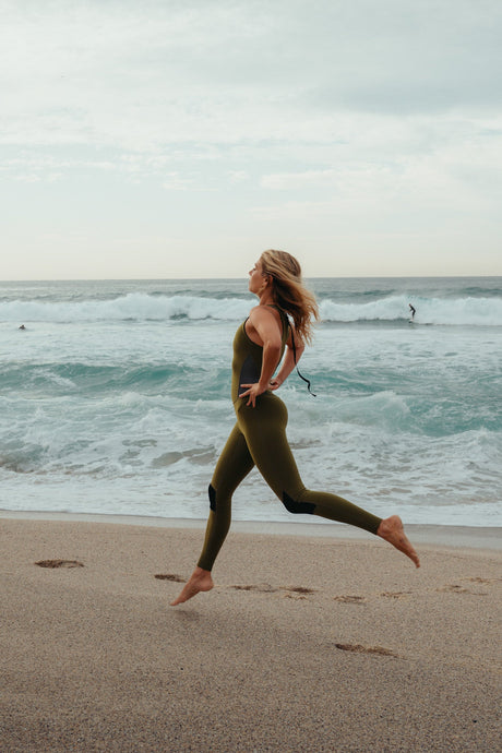 Woman running on a beach with ocean waves in the background wearing long jane