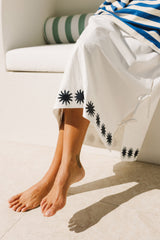 Person wearing white maxi skirt with blue sun patterns sitting on a white couch.