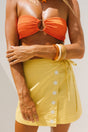 Person wearing an orange bikini top and cracker day club yellow skirt with white sun patterns on a neutral background