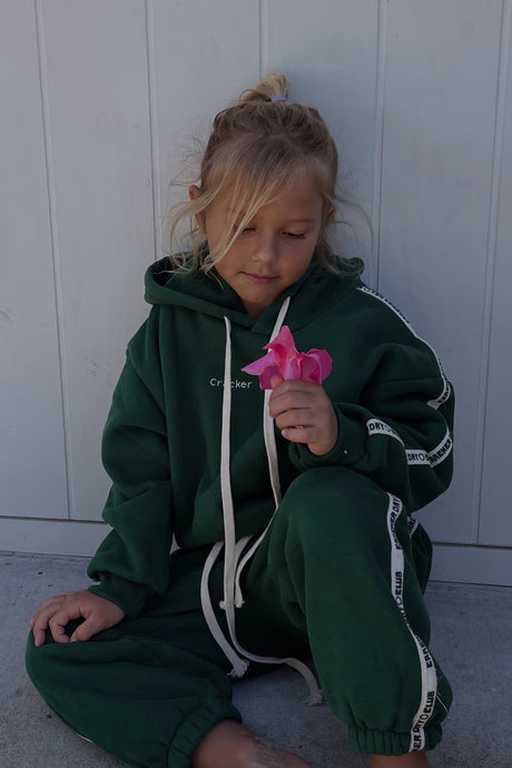 young girl wearing forest green sweatpants and sweater holding a flower by cracker day club